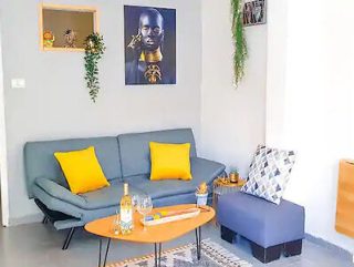 A cozy living room with a blue sofa accented with yellow pillows, a wooden coffee table, and a vibrant portrait on the wall